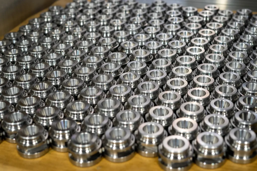 Rzędy identycznych, precyzyjnie obrobionych metalowych detali ułożonych na palecie, przykład Produkcja seryjna w obróbce CNC.