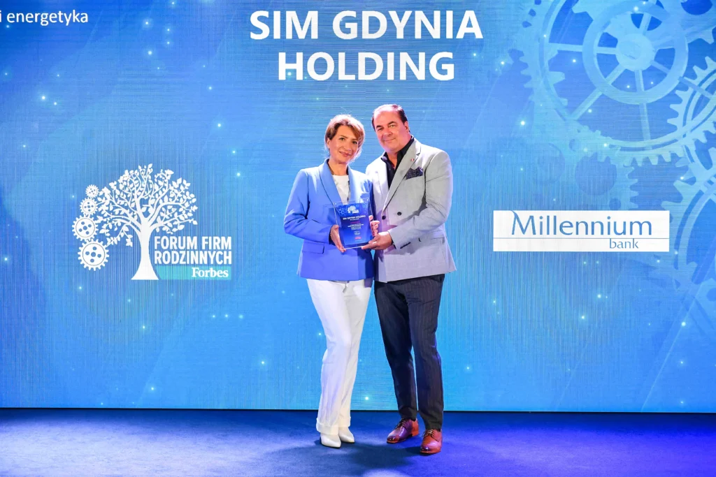 Dwie osoby pozują z nagrodą podczas gali Forum Firm Rodzinnych Forbes. W tle widoczna jest niebieska ścianka z logotypami Forbes, Millennium Bank i napisem „SIM Gdynia Holding”.